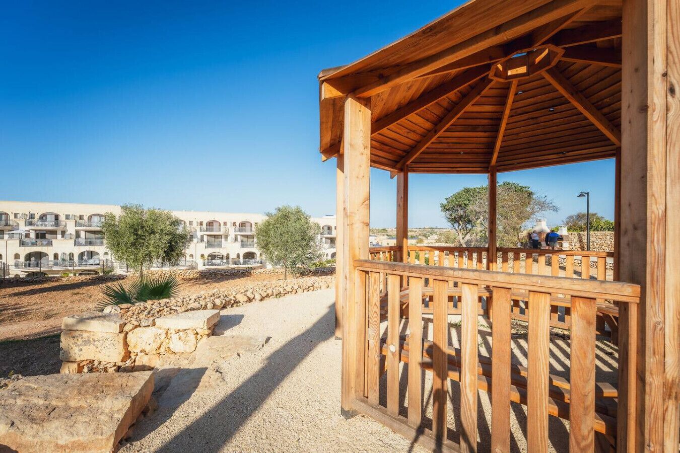 A wooden gazebo with a view of a building complex and a clear sky.