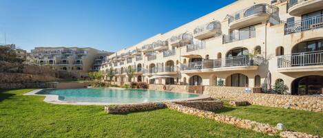 A hotel with a swimming pool surrounded by a stone wall and green grass.