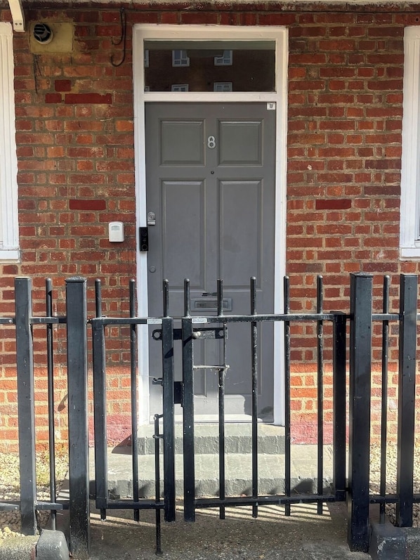 A brick building with a grey door, a metal gate, and a small window to the left.