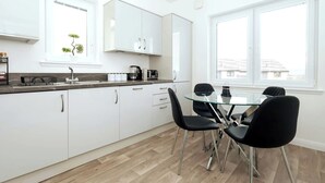 Une cuisine moderne avec des meubles blancs, un plan de travail noir et une table à manger en verre, accompagnée de quatre chaises.