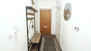 Un couloir avec un banc en bois, un téléphone fixé au mur, une porte et un thermostat.