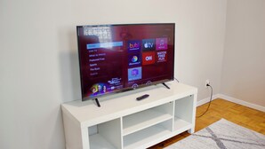 Een flatscreen televisie op een witte standaard met een afstandsbediening, voor een effen muur met een houten vloer.