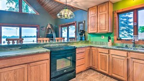 A kitchen with wooden cabinets, a black stove, and a large window overlooking a body of water.