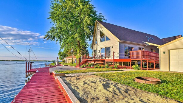 A waterfront house with a red dock, a sandy area, and a large tree.
