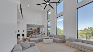 Un salon spacieux, doté d’un grand canapé d’angle, d’une table basse et offrant une vue sur l’extérieur grâce à de grandes fenêtres.