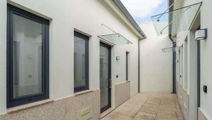 A narrow corridor with a tiled floor, a glass door, and a window with a black frame.