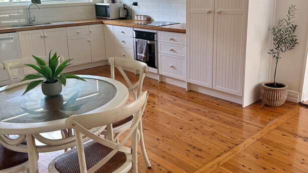 Eine moderne Küche mit weißen Schränken, einer Holz Arbeitsplatte, einem eingebauten Backofen und einem Essbereich mit einem Glastisch und weißen Stühlen.