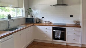 Eine Küche mit weißen Schränken, einer Holz Arbeitsplatte, einer Edelstahlspüle, einer Mikrowelle und einem Backofen.