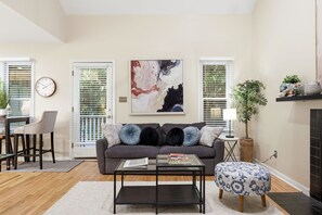 A living room with a sofa, coffee table, and ottoman, a painting on the wall, and a clock.