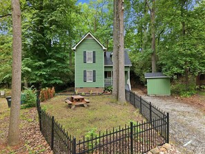 A green two-story house with a fenced yard and a small shed.