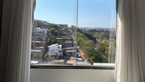 A room with a large window, curtains, and a patterned bedspread. - Cozy apartment in Muriaé (Muriaé)