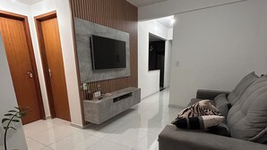 A modern living room with a flat-screen TV, a grey sofa, and a potted plant. - Cozy apartment in Muriaé (Muriaé)