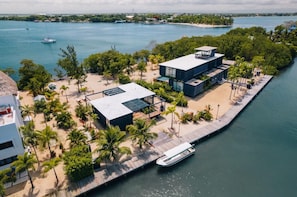 A modern waterfront property with a dock, a boat, and a beach area with palm trees. - Santosha Villa - Modern 3BR Island Villa with Pool (Placencia)