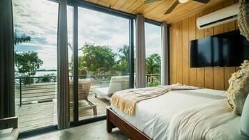 A bedroom with a large bed, a ceiling fan, a TV, and a view of the outdoors.