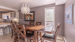Een moderne keuken met een eethoek, met een kroonluchter, houten stoelen en een groot raam.