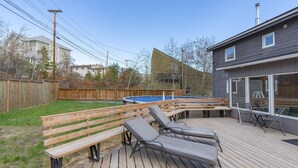 Een achtertuin met een houten terras, een zwembad en een houten bank.
