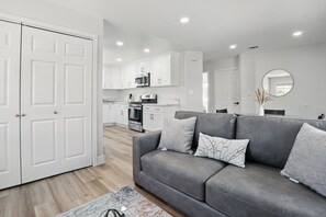 A modern living room with a grey sofa, white cabinets, and a kitchen in the background. - Cozy 2-bedroom backhouse with AC in Azusa (Azusa)