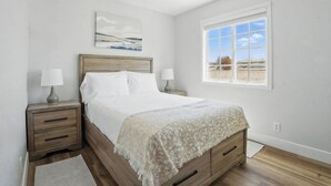 Een slaapkamer met een houten bed, twee nachtkastjes met lampen, een groot raam met uitzicht en een schilderij aan de muur.