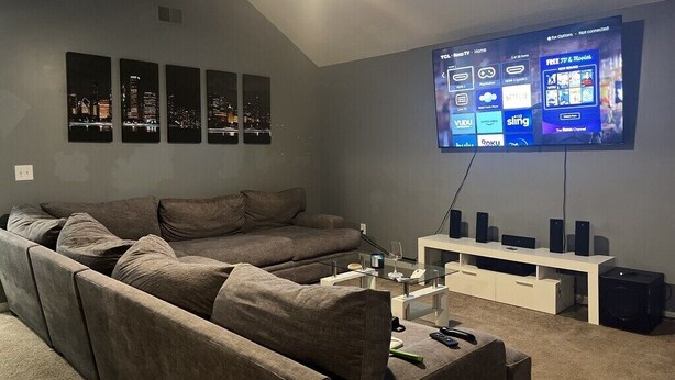 A modern living room with a sectional sofa, a flat-screen TV mounted on the wall, and a white entertainment unit with speakers. - Quiet & Cozy 3bd2bth home (Columbia)