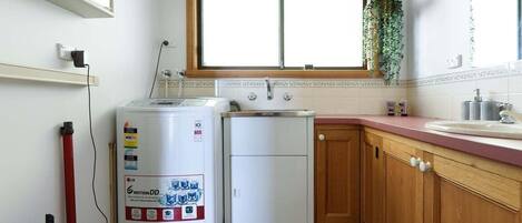 Cocina compacta con lavadora, un refrigerador pequeño y una ventana con una planta.