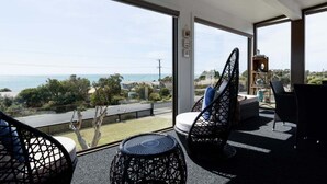 A balcony with wicker furniture, a view of the sea, and a clear sky. - Ocean View Retreat at Greens Beach (Greens Beach)