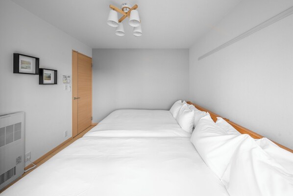 A minimalist bedroom with a large bed, a wooden wardrobe, and a ceiling light fixture. - E-US NAEBO STATION 302 (Sapporo)