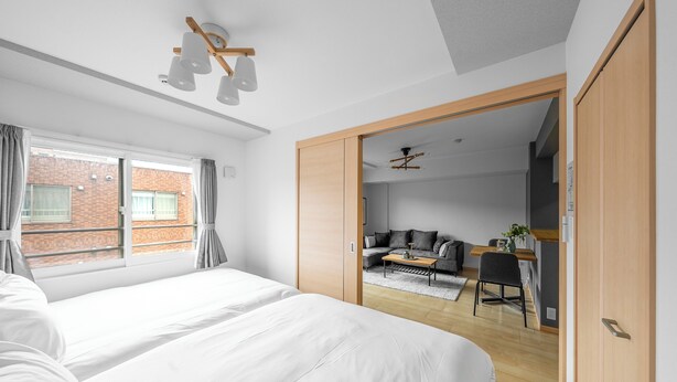 Una camera da letto moderna con un letto grande, un armadio in legno e una porta scorrevole che dà su un soggiorno con un divano e un tavolo.