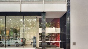 Un bâtiment moderne doté de grandes fenêtres en verre qui reflètent l’environnement, une voiture visible garée à l’extérieur et une vue dégagée sur la rue.