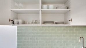 Une cuisine avec des meubles blancs, un plan de travail recouvert de carreaux verts et un évier en acier inoxydable.