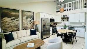 Une cuisine moderne avec des meubles blancs, un coin repas doté d’une table ronde et un salon avec un canapé et une table basse.