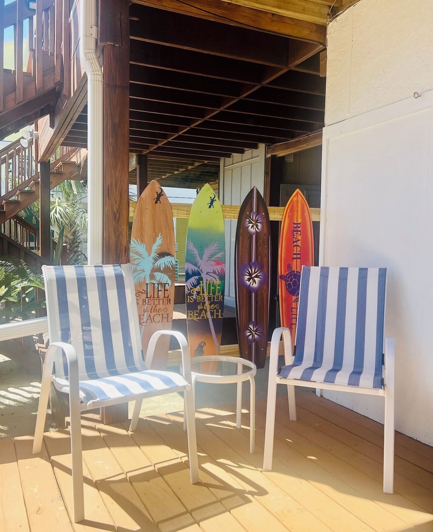 Un espacio de estar techado al aire libre con dos sillones a rayas y tres tablas de surf apoyadas en una pared.