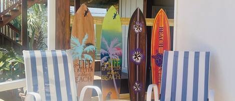 Un espacio de estar techado al aire libre con dos sillones a rayas y tres tablas de surf apoyadas en una pared.