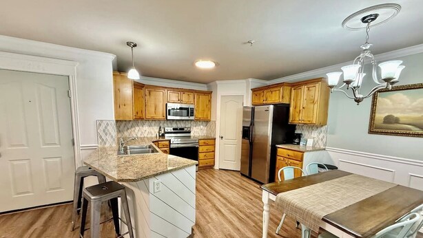 A kitchen with wooden cabinets, a granite countertop, a stainless steel refrigerator, and a dining area with a table and chairs. - The Grove Getaway-Centrally Located (Pleasant Grove)