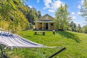 A small yellow cabin with a porch, surrounded by a grassy area and trees. - Peaceful Forest Escape by Lake Elmore (Elmore)