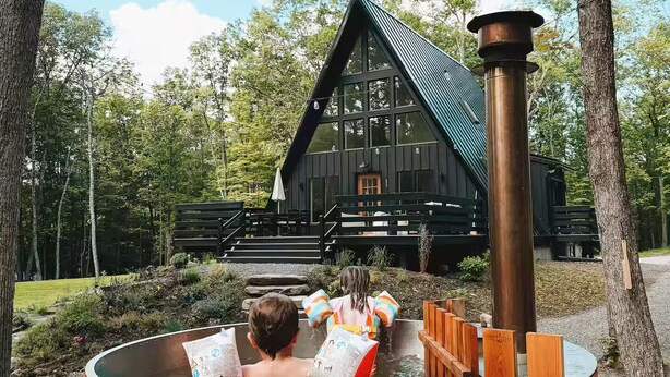 Un bain à remous en bois, avec une cabane rustique en arrière-plan.