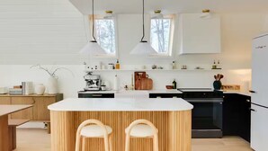 Une cuisine moderne dotée d’un îlot central, de chaises en bois, de luminaires suspendus et d’un four encastré.