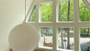 Une pièce dotée d’un plafond en pente, de poutres en bois et de grandes fenêtres donnant sur la forêt.