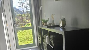 A modern room with a sliding glass door leading to a balcony, a built-in shelf with towels, and a small potted plant. - Pakihi Retreat (Toatoa)