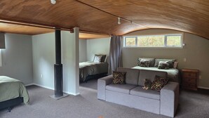 A cozy attic bedroom with a sloped ceiling, a bed, a sofa, and a window. - Pakihi Retreat (Toatoa)