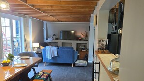 A cozy living area with a wooden ceiling, a blue sofa, a dining table with benches, and a kitchen area with a TV and various kitchen items. - Pakihi Retreat (Toatoa)