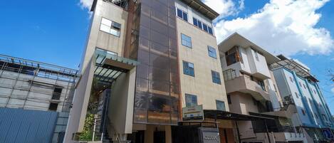 A multi-story hotel with a modern design, featuring a prominent glass facade, a staircase leading to the entrance, and a sign indicating fitness facilities.