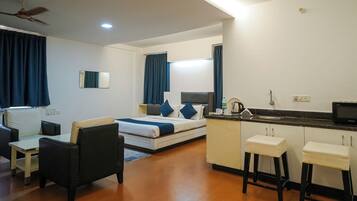 Habitación de hotel moderna con cama, escritorio, silla, kitchenette y ventilador de techo.