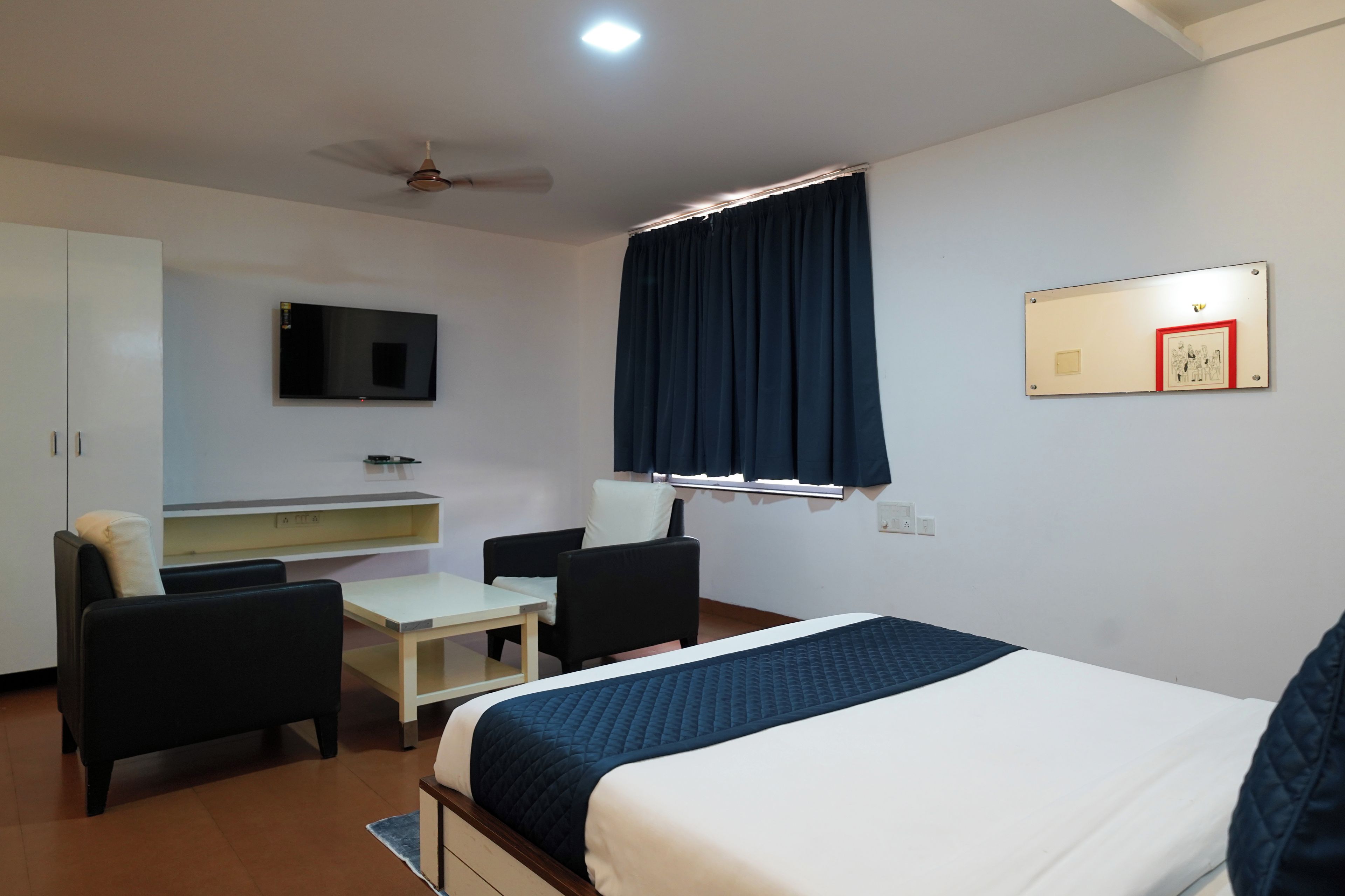 A hotel room with a bed, a desk, a chair, a television, and a ceiling fan.
