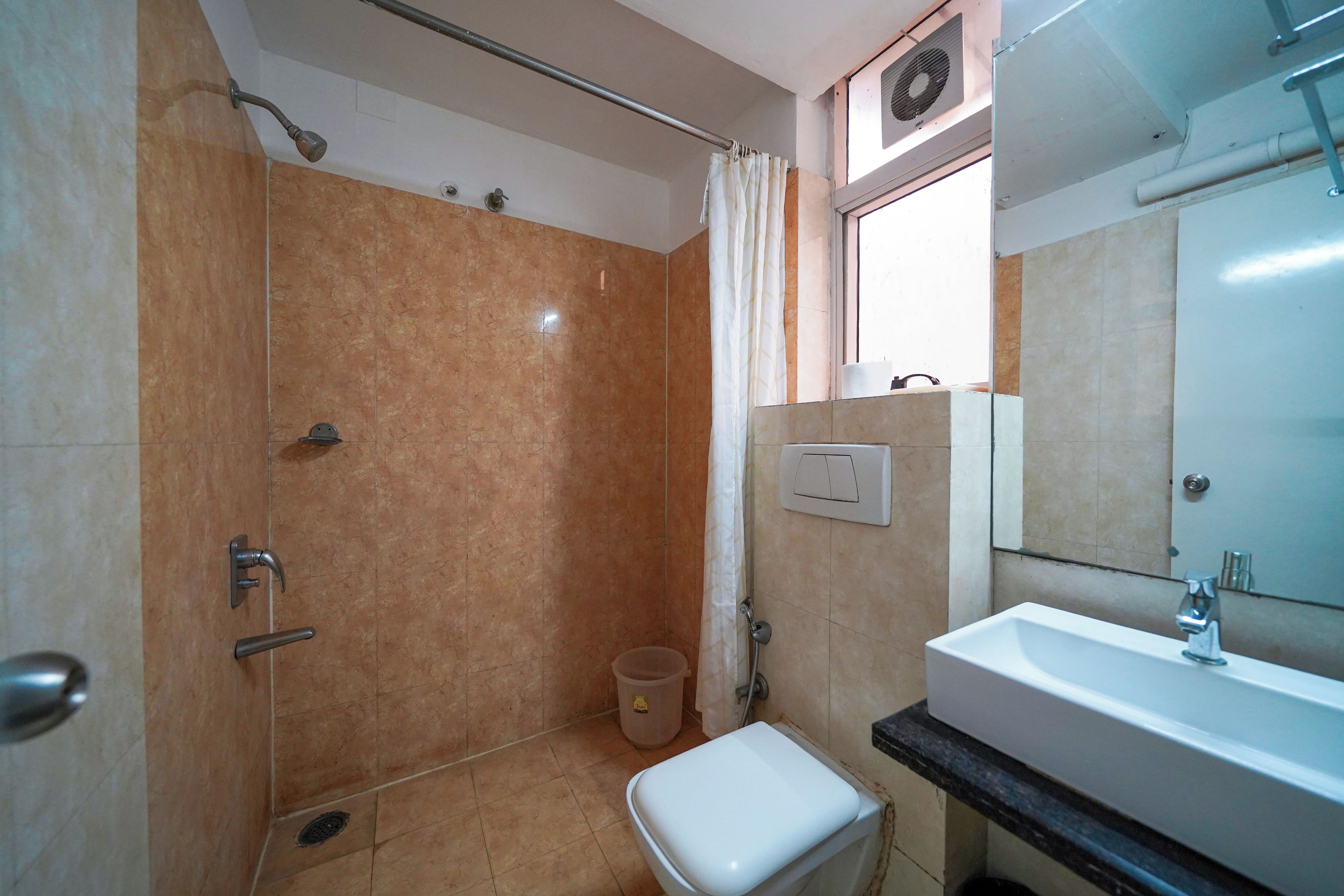 Een badkamer met douche, toilet, wastafel en een raam met gordijn.