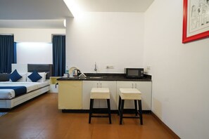 A compact hotel room with a bed, a kitchenette, and a small bar area. - VH Hotels Domlur (Bengaluru)