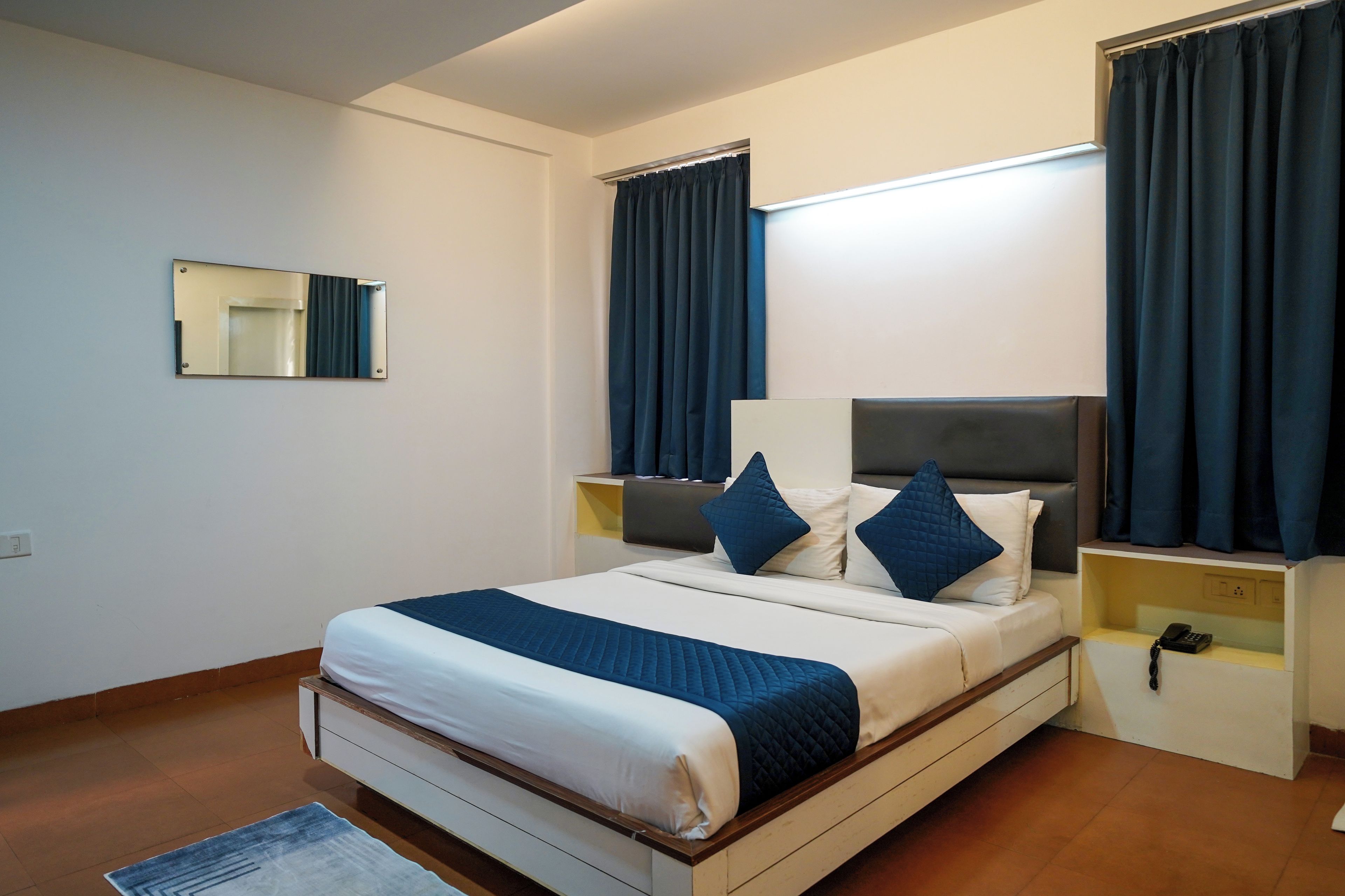 Una habitación de hotel con una cama, mesitas de noche, un espejo y cortinas.