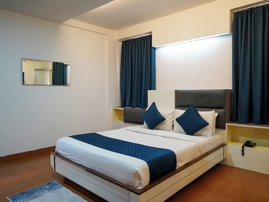Una habitación de hotel con una cama, mesitas de noche, un espejo y cortinas.