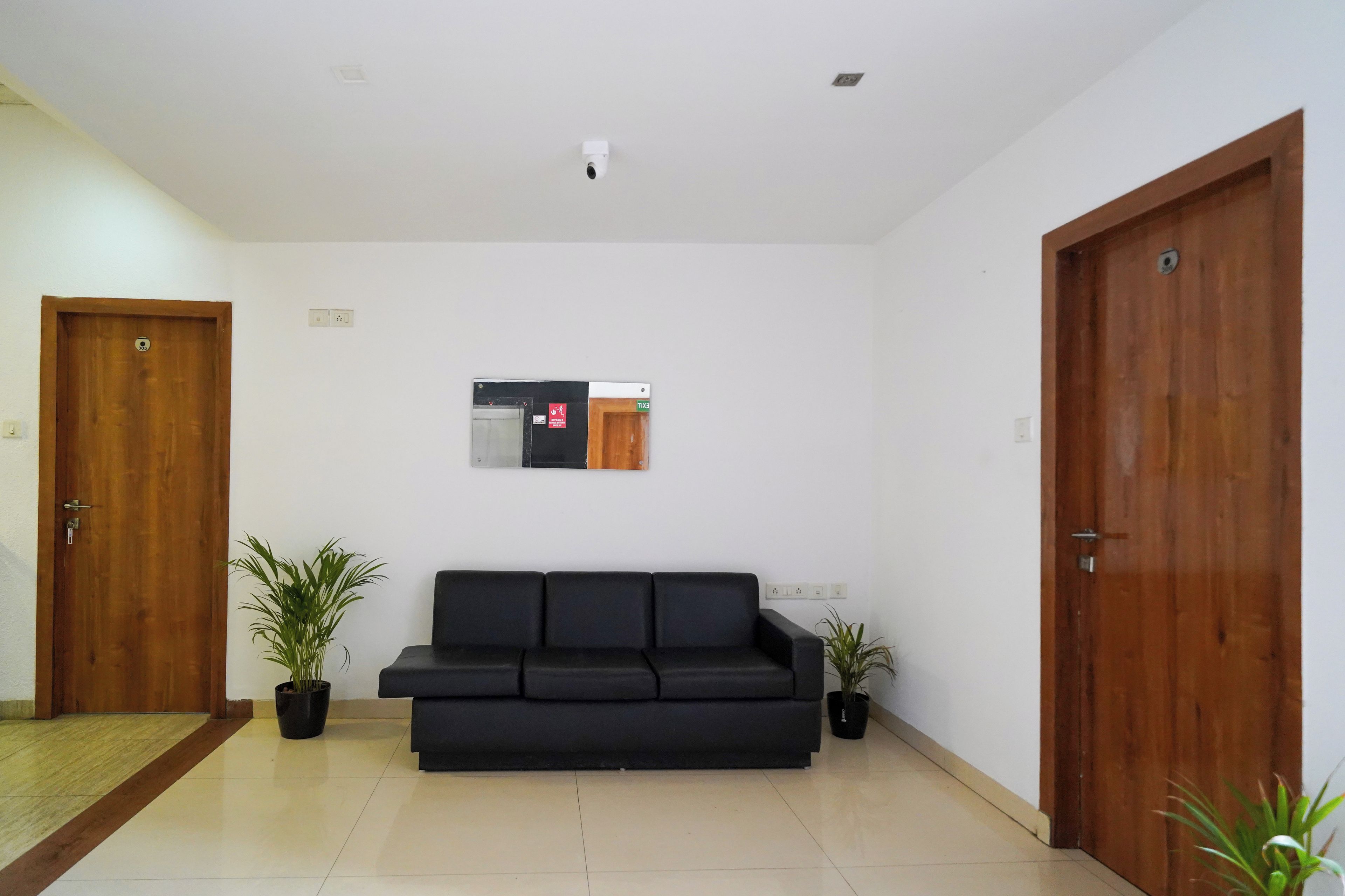 A room with a black sofa, two potted plants, wooden doors, and a wall-mounted sign.