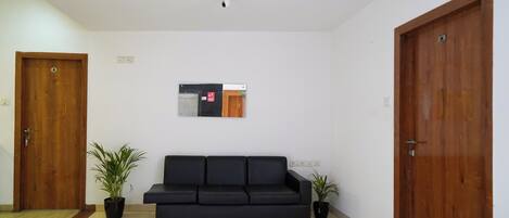 A room with a black sofa, two potted plants, wooden doors, and a wall-mounted sign.