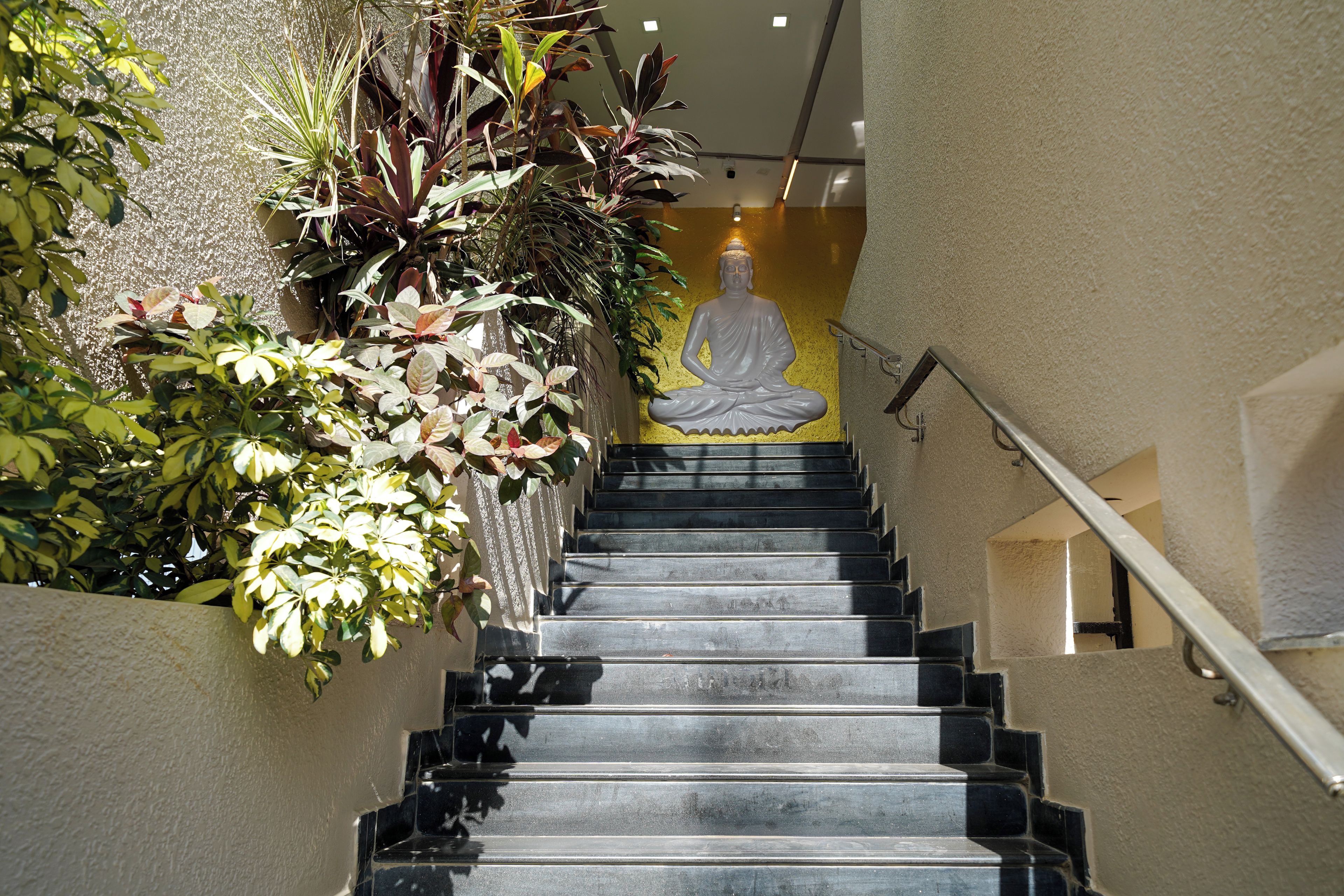 A staircase with a Buddha statue at the top, surrounded by lush greenery.